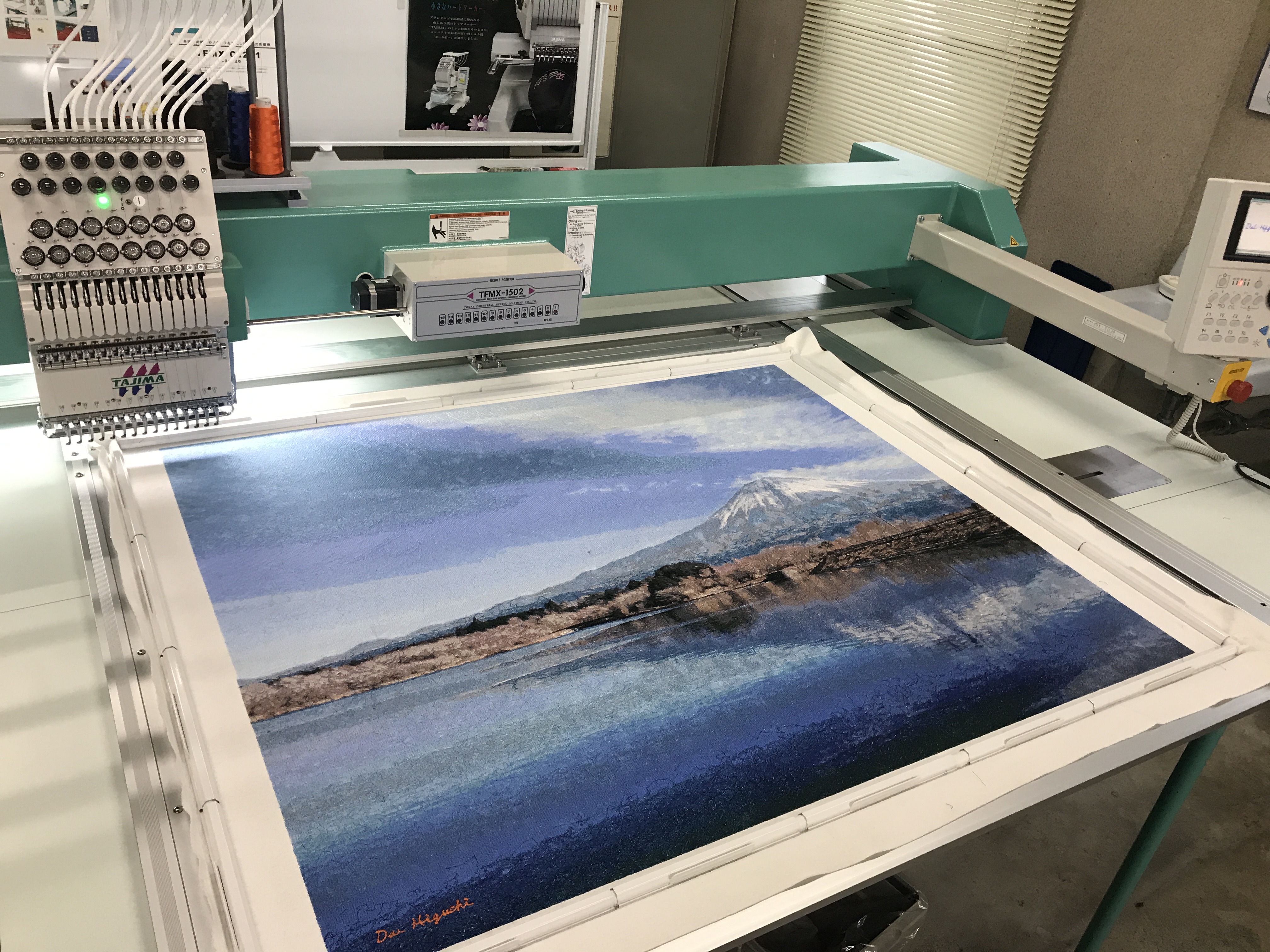 フォト刺繍作品の制作風景。工業用刺繍機で風景写真の光と陰影を糸で再構成している様子