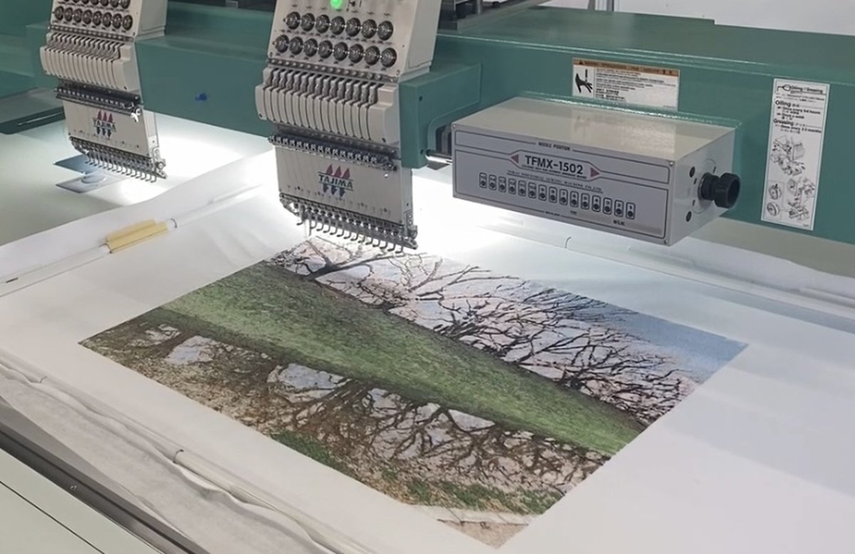 大型タジマ刺繍機で、背割堤の桜並木をモチーフにしたフォト刺繍作品を縫製している様子。緻密なステッチで春の風景を表現。