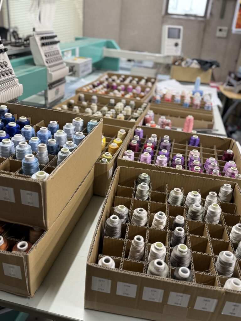 日本語： タジマ刺繍機と、フォト刺繍制作に使う数百色の刺繍糸。作品表現の幅を広げるための必須の環境。