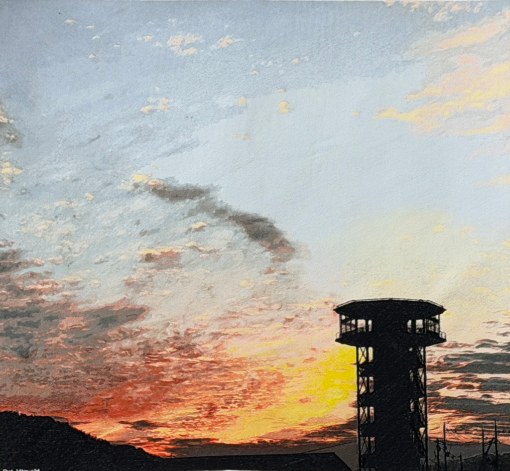 夕暮れのさくらであい館(京都府・八幡市)を描いたフォト刺繍作品。燃えるような黄・橙・赤に染まる空を背景に、展望タワーのシルエットが浮かぶ。工業用タジマ刺繍機を用いて手作業で制作。Dal Higuchi、2026年。